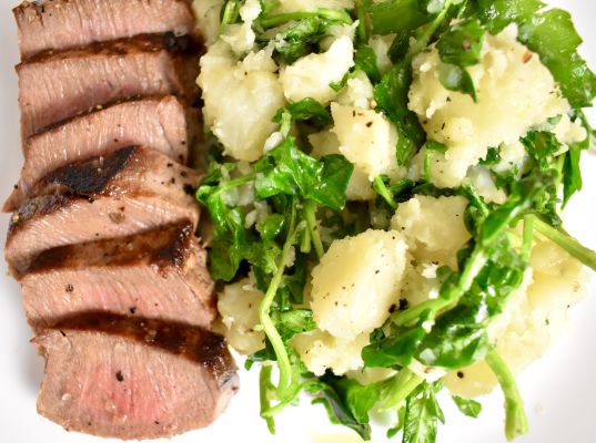 Grilled venison steak served with potato salad and greens.