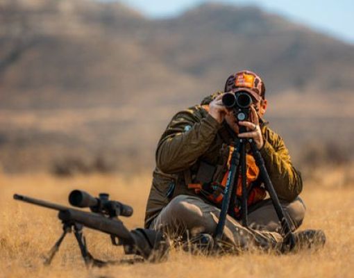 Hunter using a spotting scope in a mountain landscape.
