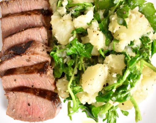 Grilled venison steak served with potato salad and greens.