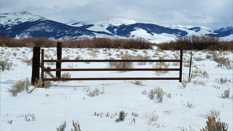 Snowy landscape with a wooden fence in a mountainous area.