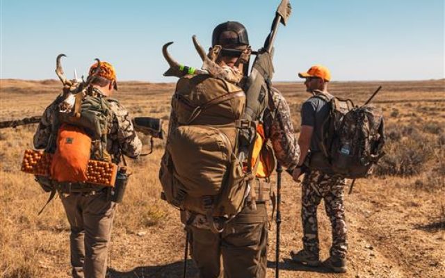Hunters walking through a desert landscape with gear during a hunting expedition.