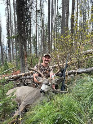 Hunter with mule deer in a forest setting.