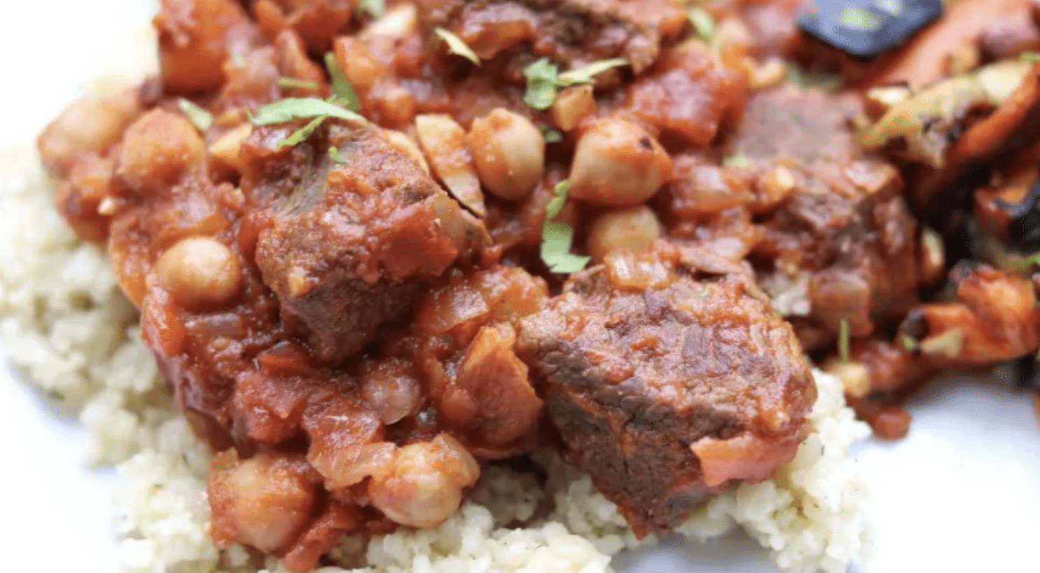 Venison stew served over grain, garnished with herbs.