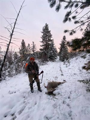 Hunter standing by mule deer in snowy forested area.