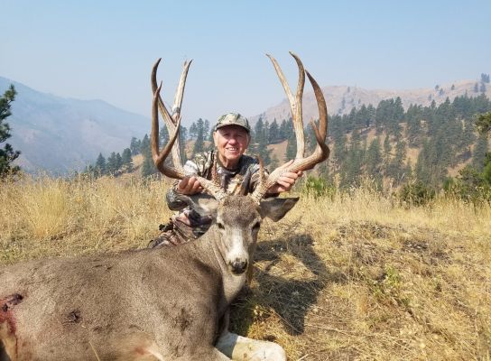 Hunter with a mule deer buck in a mountain setting.