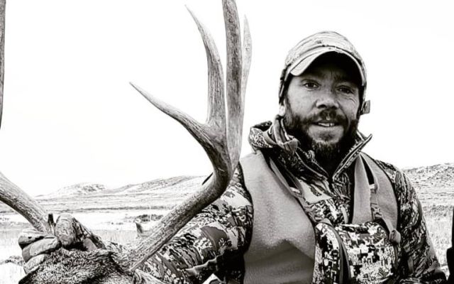 Hunter posing with a mule deer in a natural setting.