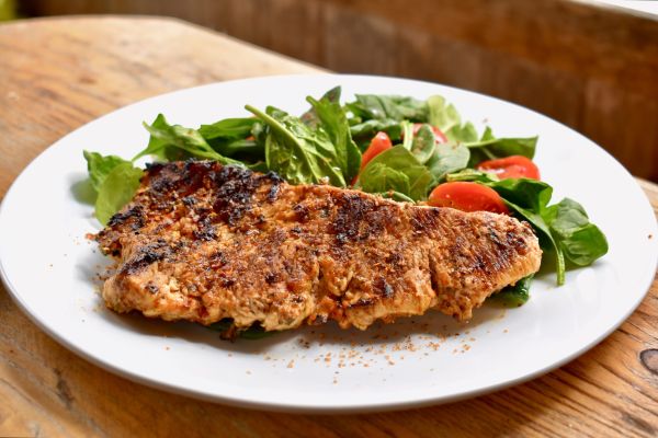 Grilled fish filet served on a plate with fresh spinach and tomato salad.
