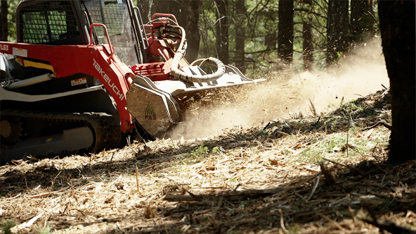 Land clearing machine in a forested area, creating dust and debris.