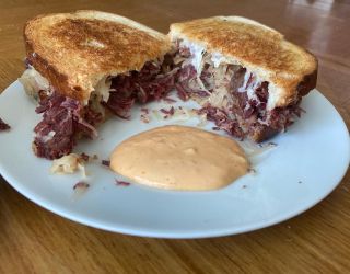 Corned beef sandwich with sauerkraut and dipping sauce on a white plate.