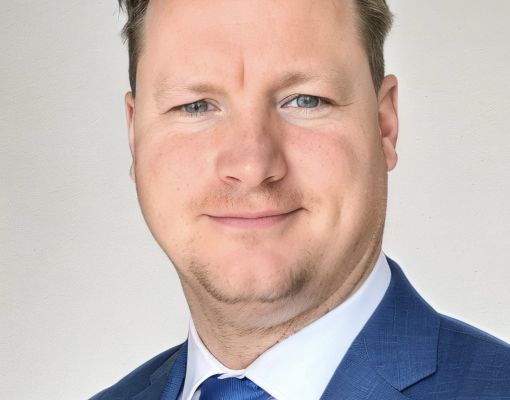 Professional headshot in business attire with blue suit and tie.