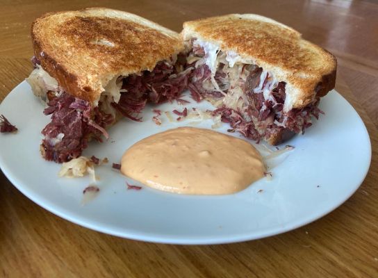 Corned beef sandwich with sauerkraut and dipping sauce on a white plate.