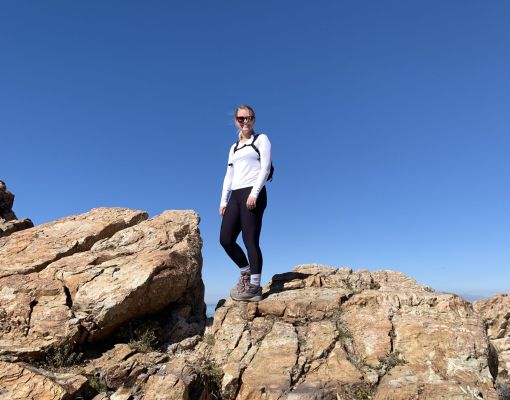 Hiker standing on rocky terrain under clear blue sky.