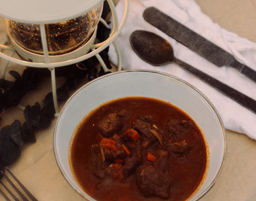 Bowl of deer meat stew with lantern and utensils in camp setting.