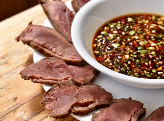 Slices of venison served with a flavorful dipping sauce on a wooden table.