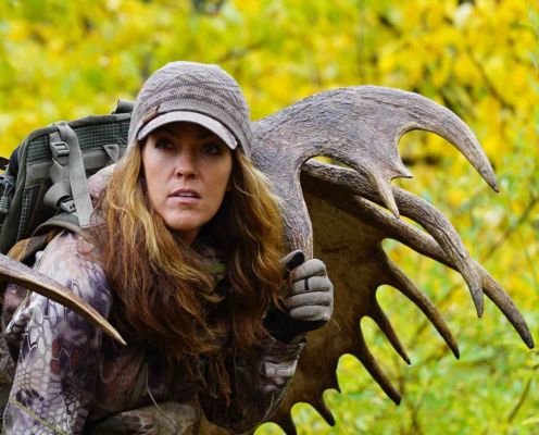 Woman hunter carrying moose antlers in vibrant autumn landscape.