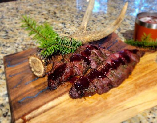 Plate of venison with antler decoration on wooden cutting board.