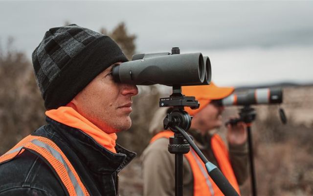 Hunters observing wildlife with binoculars in a natural setting.