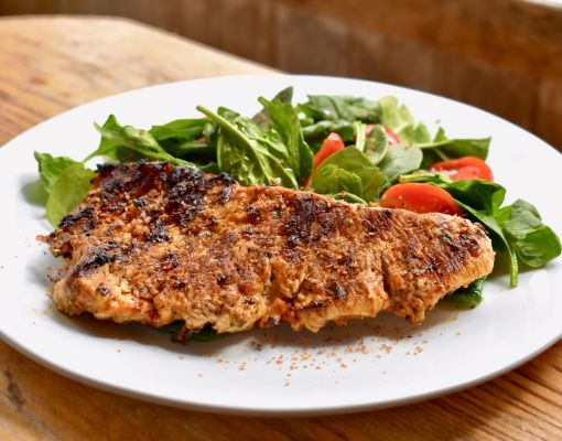 Grilled fish filet served on a plate with fresh spinach and tomato salad.