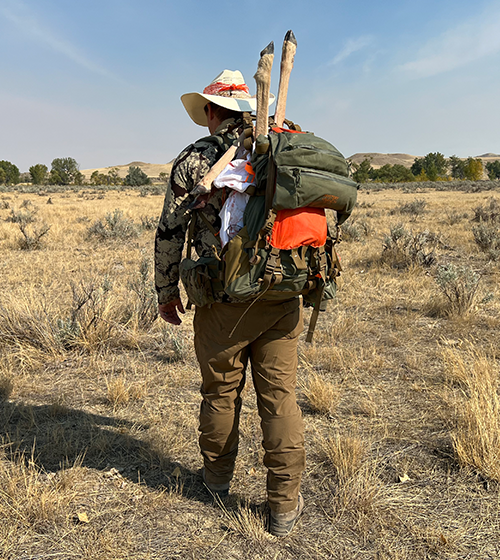 Hunter in a grassy field with a backpack and hat