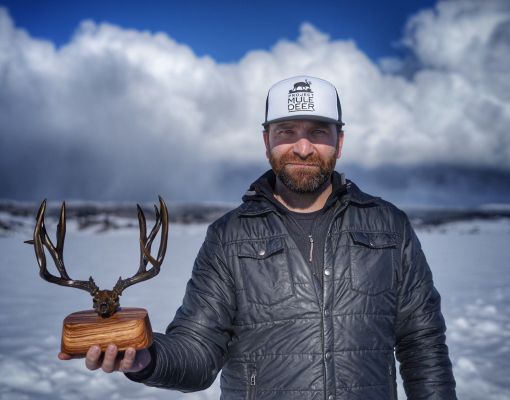 Man holding mule deer antlers trophy in snowy setting