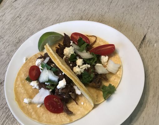 Tacos topped with vegetables and cheese on a white plate.