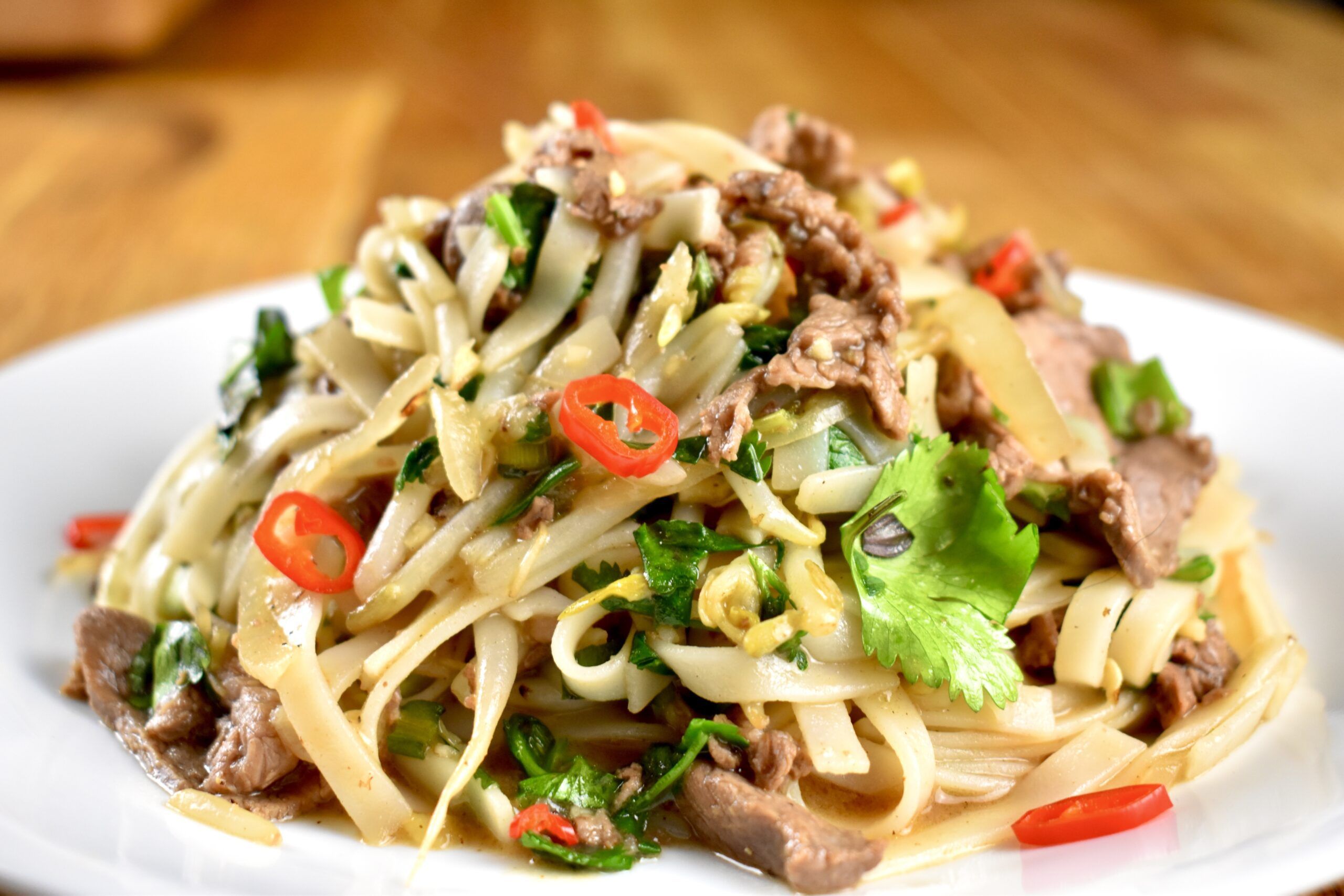 Plate of stir-fried noodles with beef, cilantro, and chili slices.