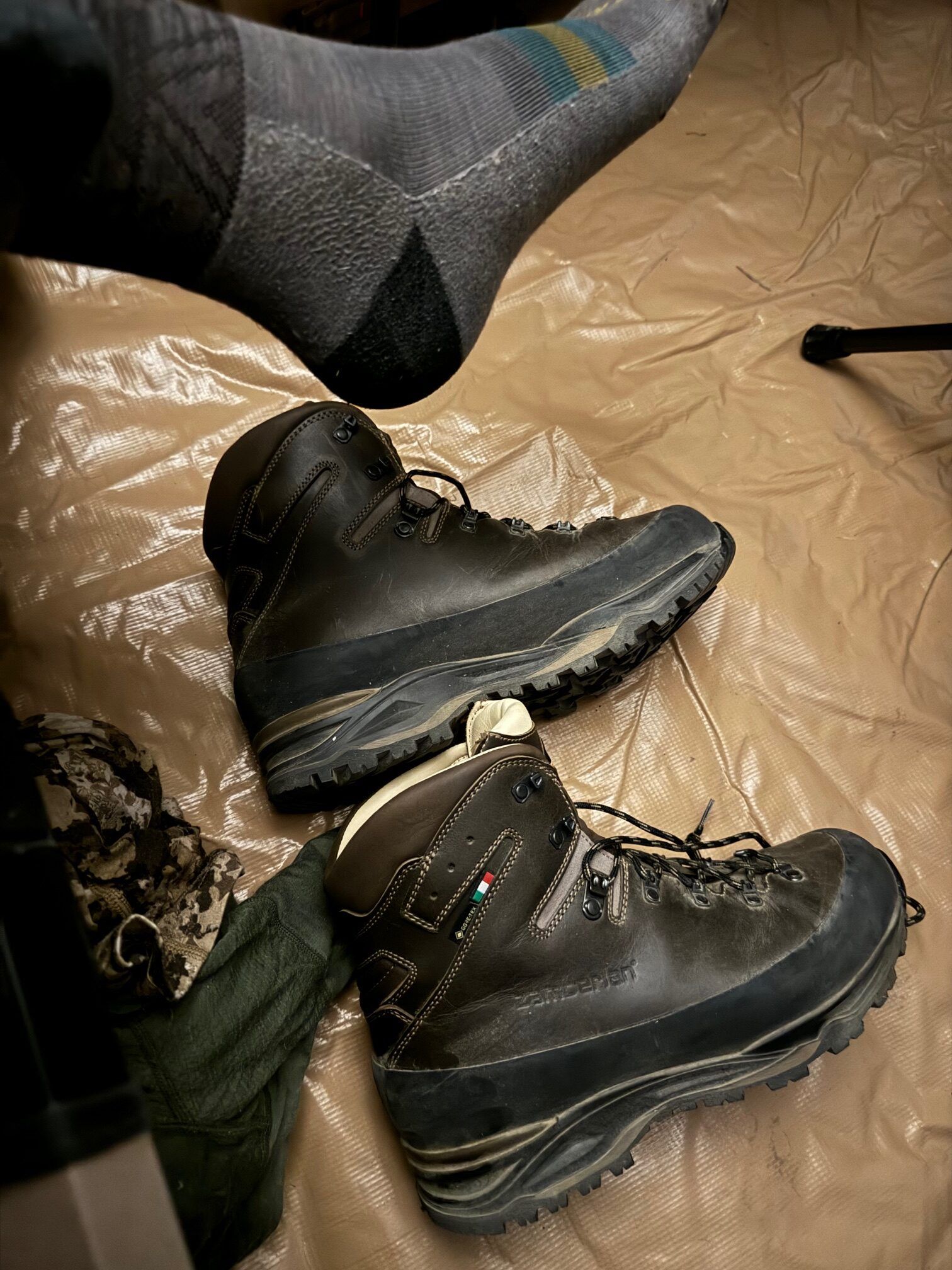 Hiking boots next to a foot in a sock on a camp floor