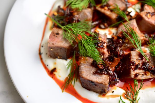Plated venison dish garnished with herbs and sauce.