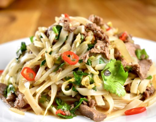 Plate of stir-fried noodles with beef, cilantro, and chili slices.