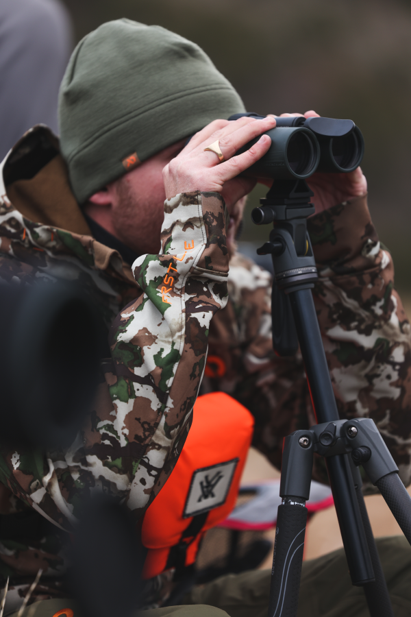 Hunter observing wildlife through binoculars in a natural setting.