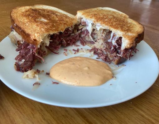 Corned beef sandwich with sauerkraut and dipping sauce on a white plate.