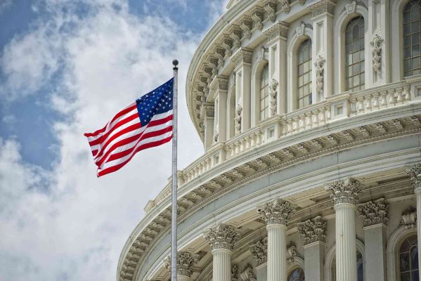 U.S. Capitol Building with American flag against cloudy sky.