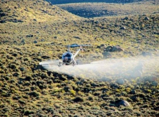 Helicopter applying spray over a mountainous area.