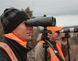 Hunters observing wildlife with binoculars in a natural setting.