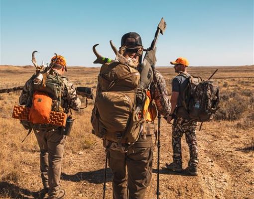 Hunters walking through a desert landscape with gear during a hunting expedition.