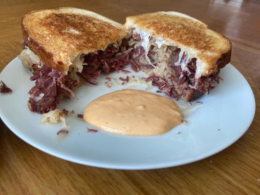 Corned beef sandwich with sauerkraut and dipping sauce on a white plate.