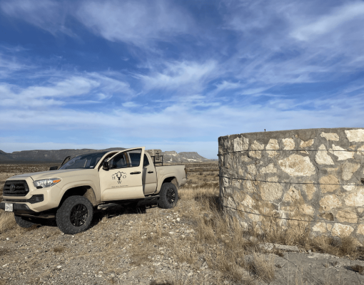 Pick-up truck near water storage in open desert landscape.