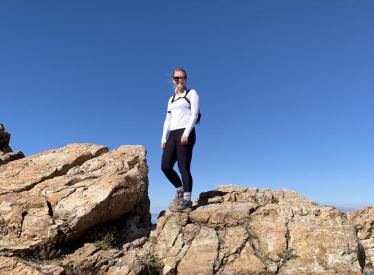 Hiker standing on rocky terrain under clear blue sky.
