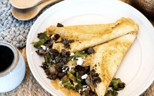 Savory crepe filled with meat and greens on a plate.
