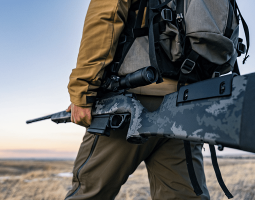 Hunter with rifle in a field during sunset.