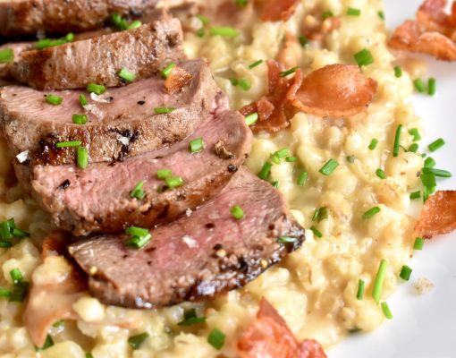 Sliced mule deer steak served with rice and garnished with chives.