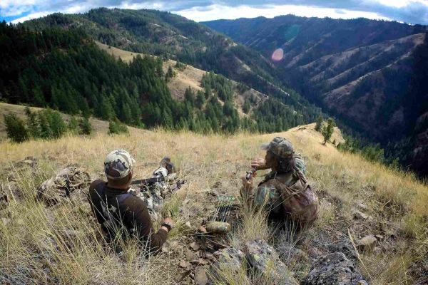 two hunters resting on a grassy hill overlooking mountain landscape