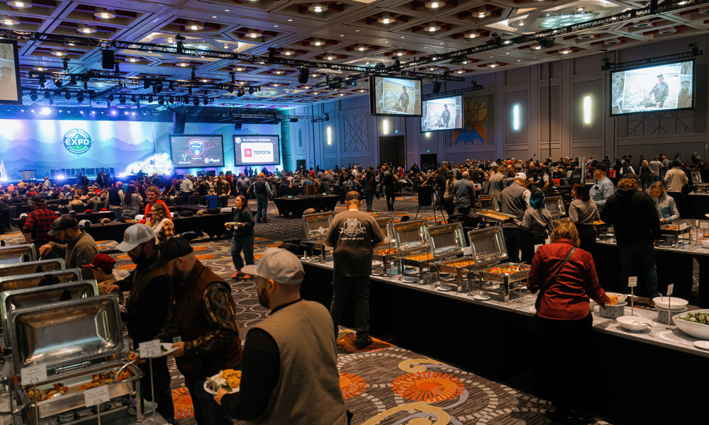 Diverse crowd dining at an expo event with a stage in the background.