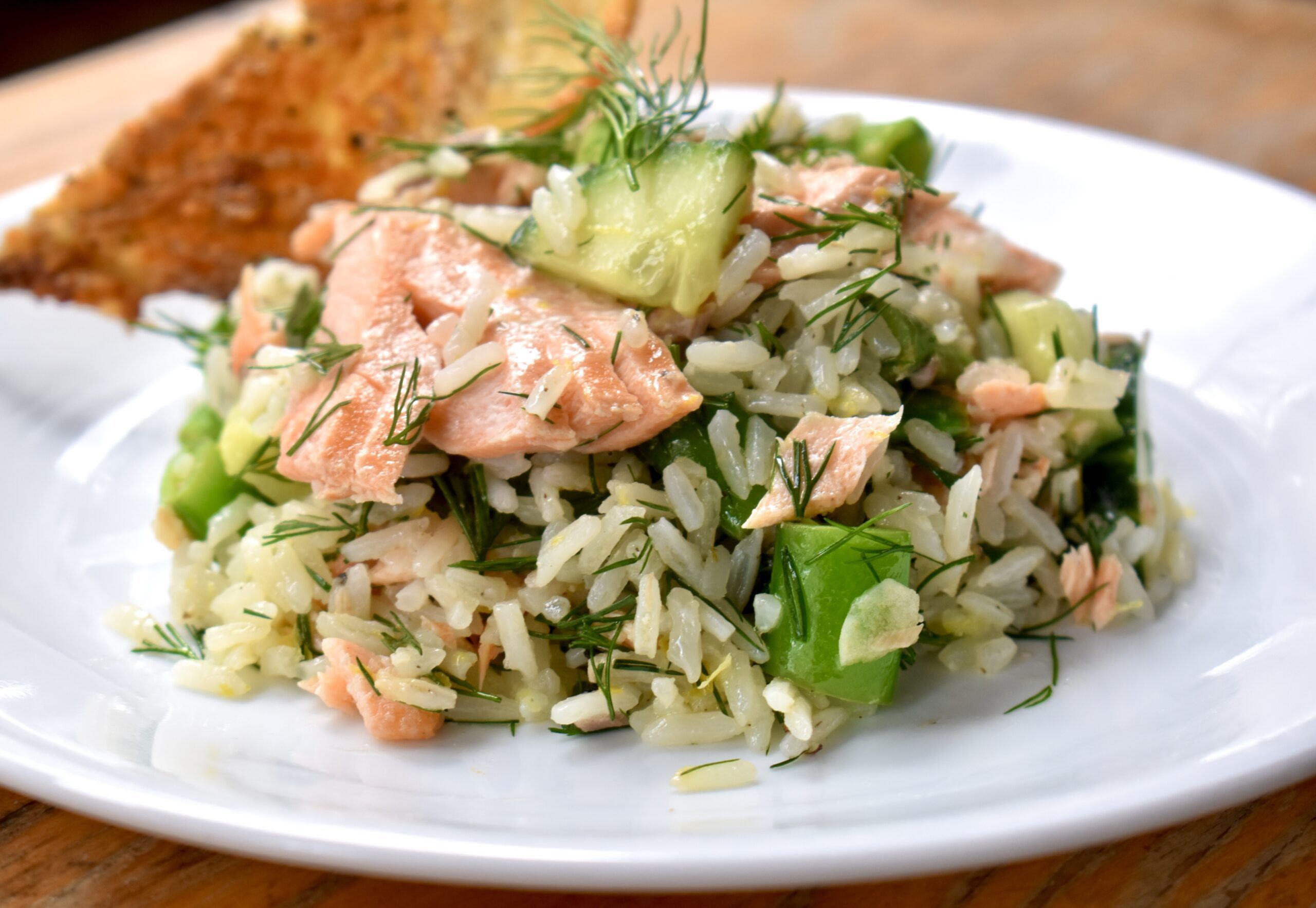 Salmon rice salad served on a white plate with a slice of toasted bread.