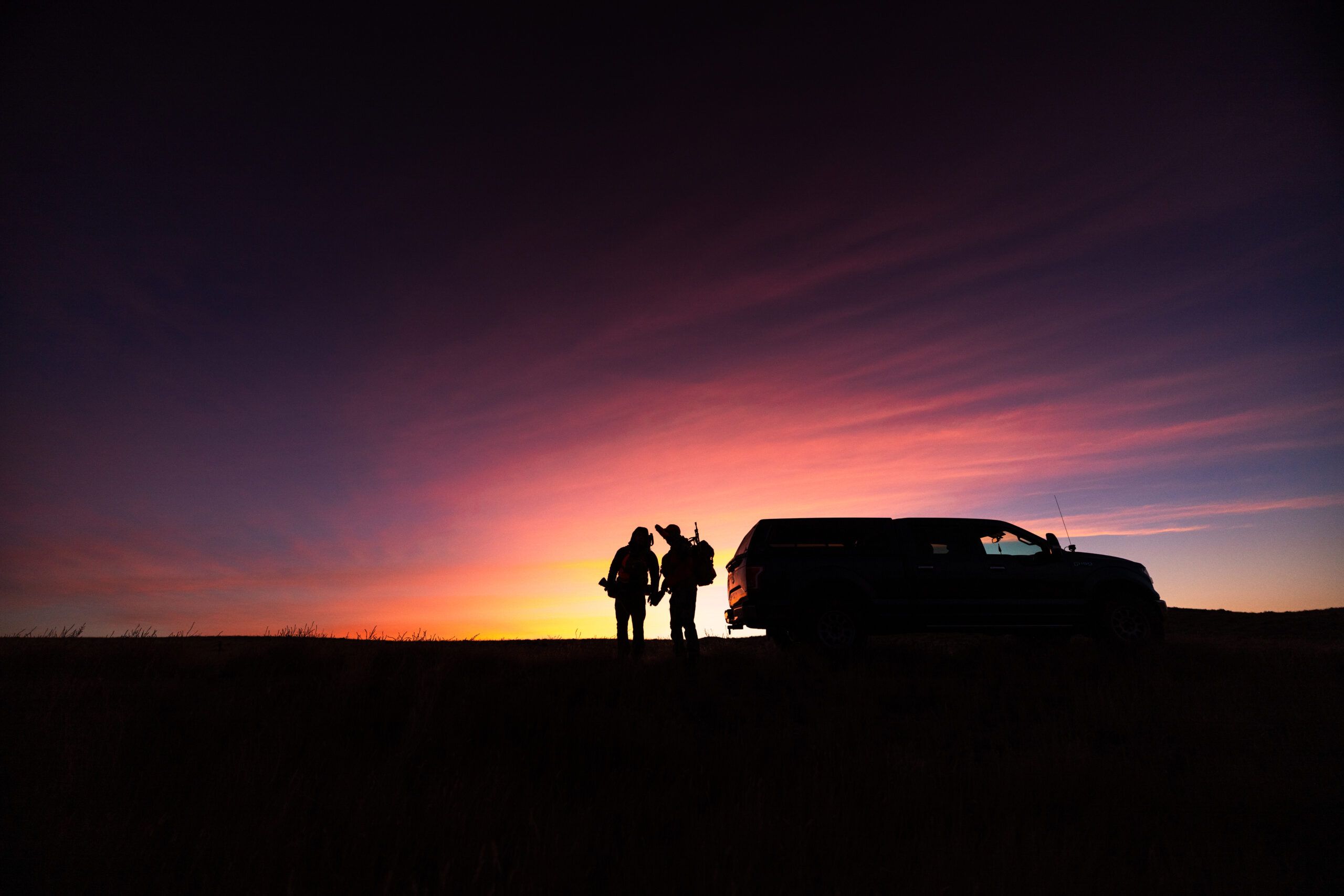 Silhouettes of a hunting party at sunset with a vehicle
