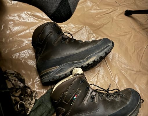 Hiking boots next to a foot in a sock on a camp floor