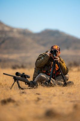 Hunter using a spotting scope in a mountain landscape.