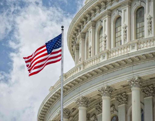 U.S. Capitol Building with American flag against cloudy sky.