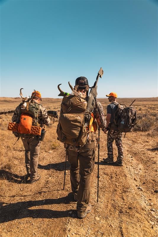 Hunters walking through a desert landscape with gear during a hunting expedition.