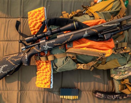 Hunting gear including a rifle, backpack, and ammunition on a padded surface.